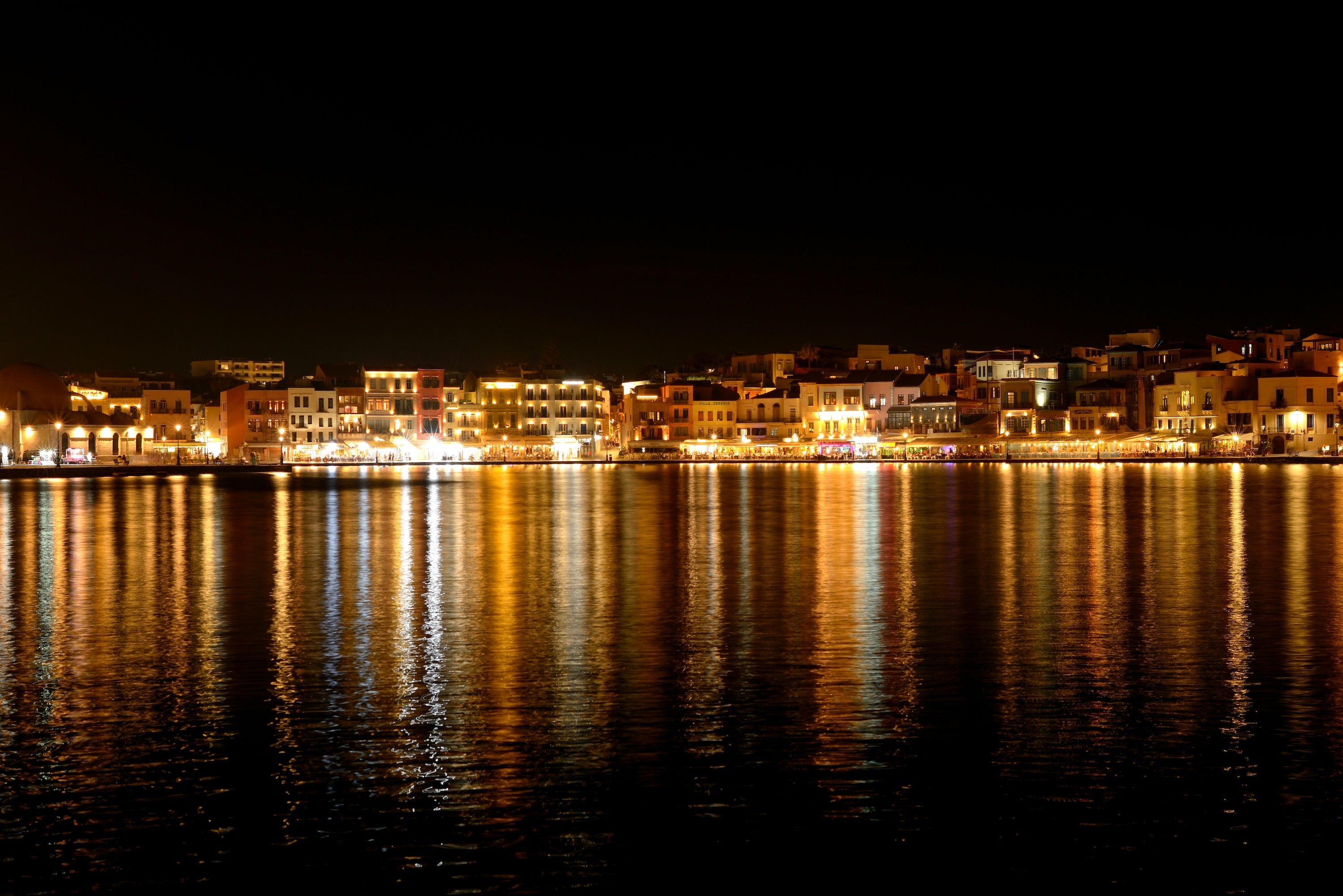 Lichter der Promenade einer Hafenstadt spiegeln sich im Wasser.