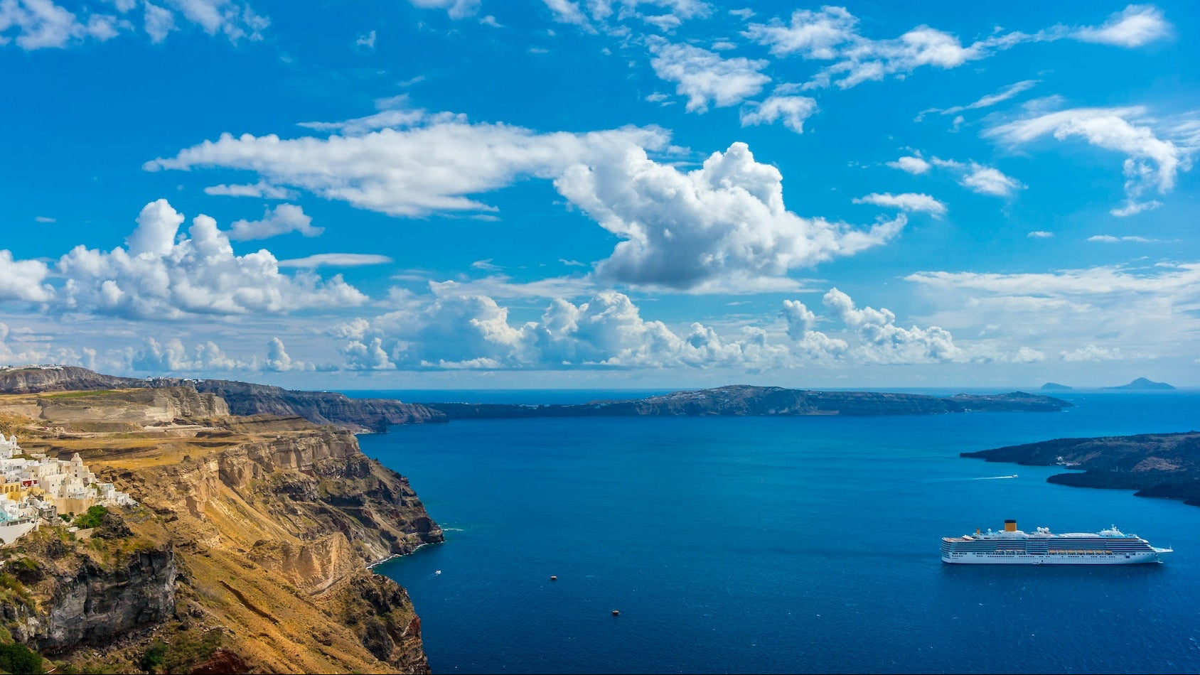 Kreuzfahrtschiff vor der felsigen Küste und den weißen Häusern von Santorin