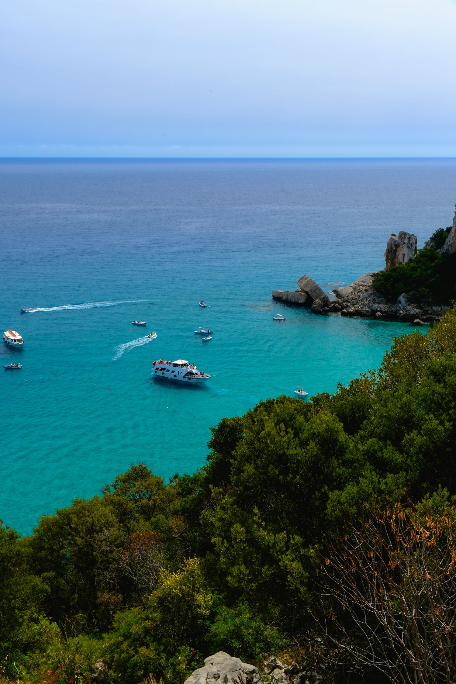 Boote auf türkisfarbenem Wasser vor der Felsenküste Sardiniens